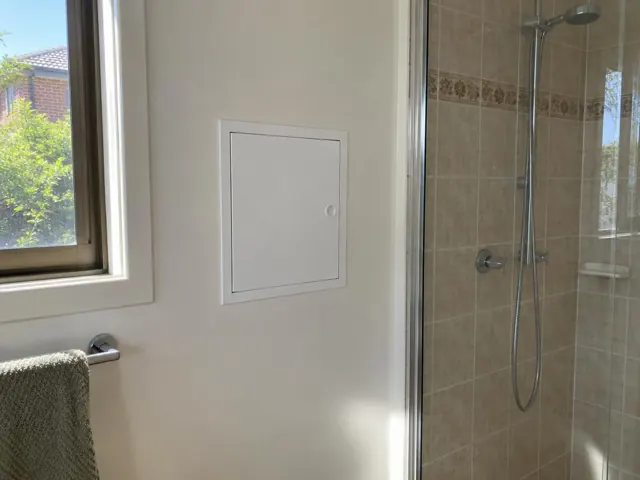 Bathroom wall with a small access panel beside a shower and window in Kotara